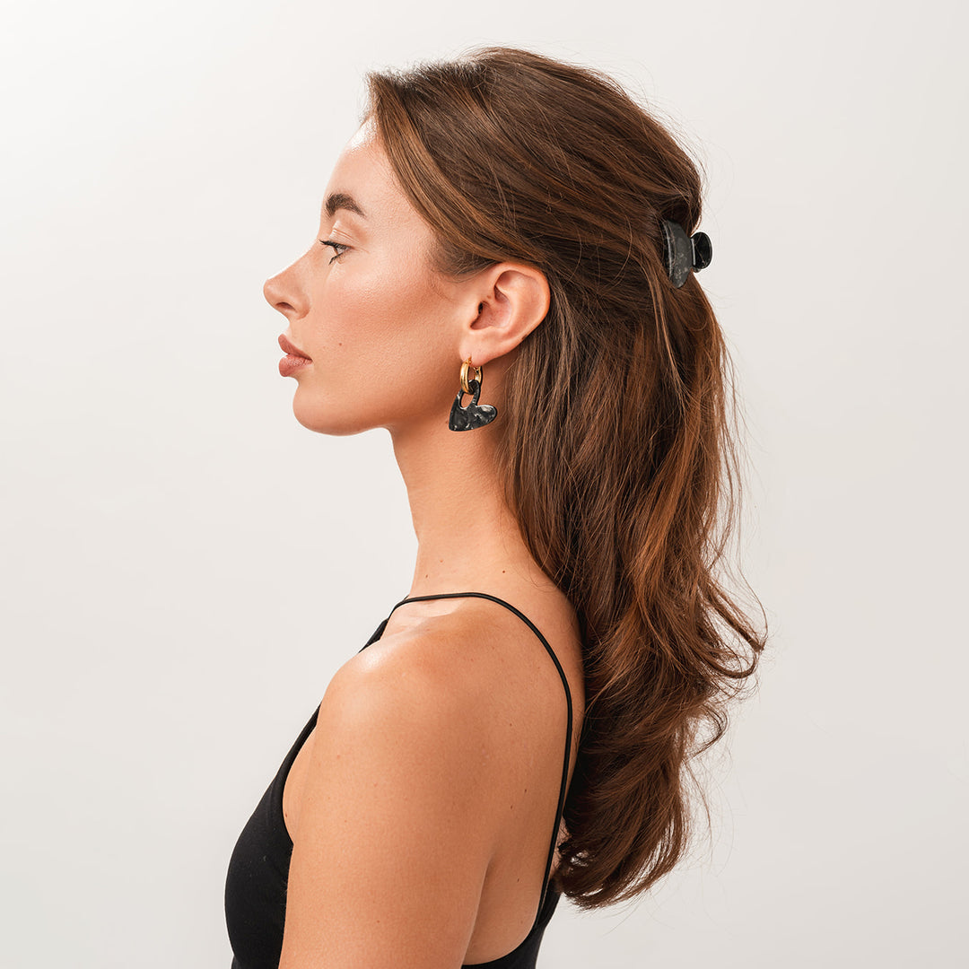 Model met bruin haar die de Love oorbellen draagt in de kleur Midnight Pearl met een bijpassende kleine klem.